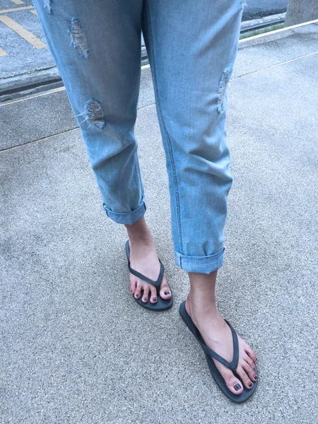 De cerca en los pies de la muchacha con sandalias negras y pantalones vaqueros azules en la calle —  Fotos de Stock