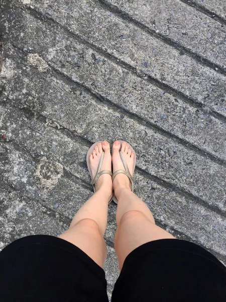 Kvinnliga fötter i guld sandaler och svarta byxor på gatan — Stockfoto