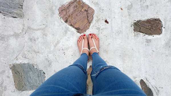 Gros plan sur les pieds de fille portant des sandales et des jeans bleus sur le ciment — Photo