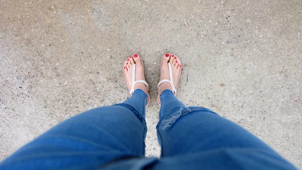 在水泥上穿凉鞋和蓝色牛仔裤的女孩脚上特写 — 图库照片