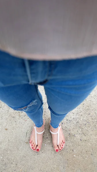 De cerca en los pies de la muchacha con sandalias y pantalones vaqueros azules en el cemento —  Fotos de Stock