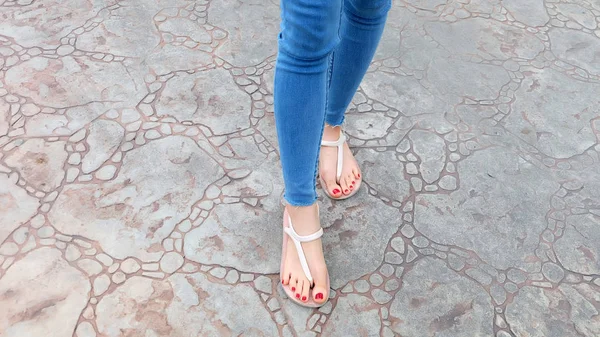 Zamknąć na dziewczęce nogi nosić sandały i niebieskie dżinsy na płytki — Zdjęcie stockowe