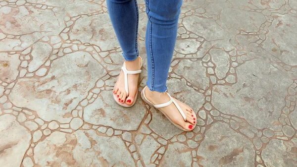 Närbild på flickans fötter bär sandaler och blå Jeans på kakel — Stockfoto