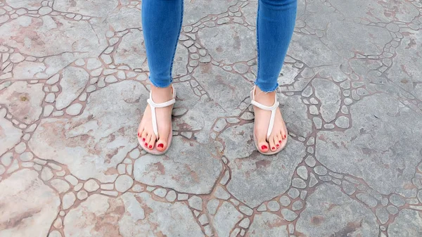 Крупним планом на ноги дівчата носити сандалі і сині джинси на плитці — стокове фото