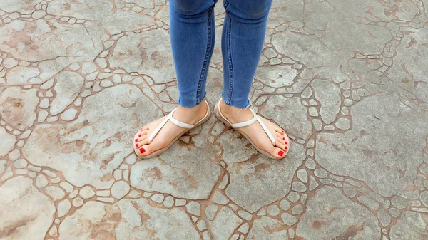 De cerca en los pies de la muchacha con sandalias y pantalones vaqueros azules en el azulejo —  Fotos de Stock