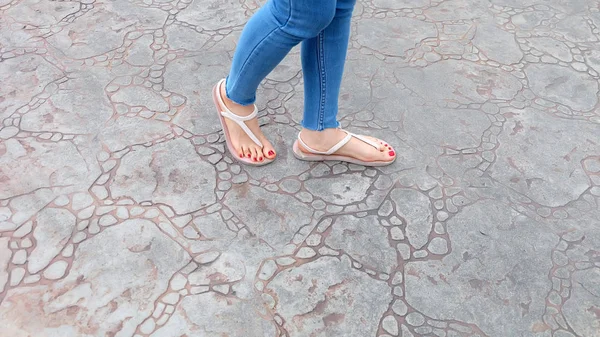 De cerca en los pies de la muchacha con sandalias y pantalones vaqueros azules en el azulejo — Foto de Stock