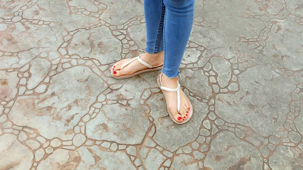 Närbild på flickans fötter bär sandaler och blå Jeans på kakel — Stockfoto