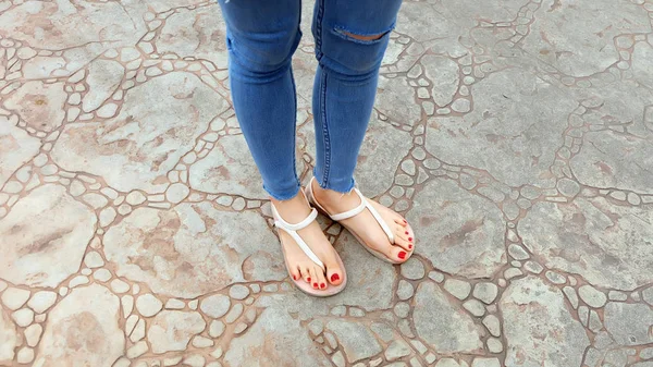 Närbild på flickans fötter bär sandaler och blå Jeans på kakel — Stockfoto