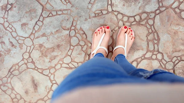 Gros plan sur les pieds de la fille portant des sandales et des jeans bleus sur la tuile — Photo