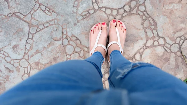 在女孩的脚上特写穿着凉鞋和蓝色牛仔裤在瓷砖上 — 图库照片
