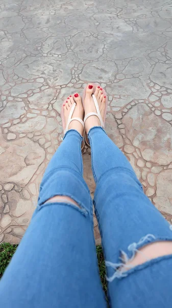 Gros plan sur les pieds de la fille portant des sandales et des jeans bleus sur la tuile — Photo