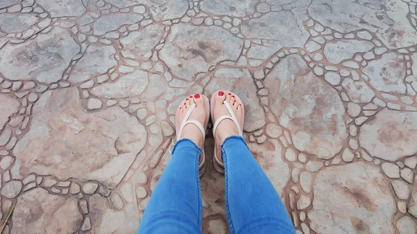 De cerca en los pies de la muchacha con sandalias y pantalones vaqueros azules en el azulejo — Foto de Stock