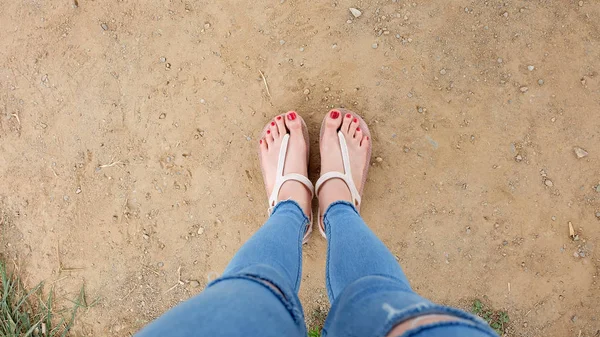 在土壤背景下, 亲密的女孩脚上穿着凉鞋和红指甲 — 图库照片