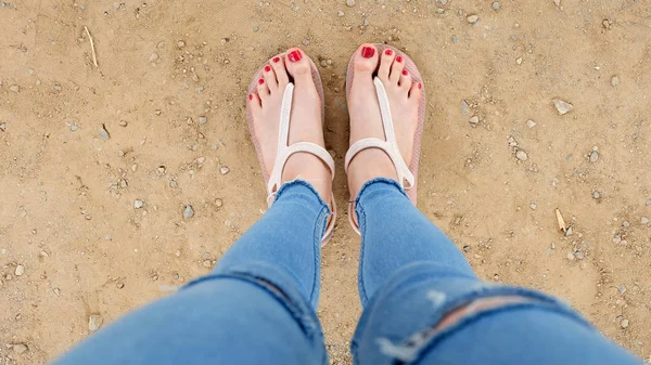 Närbild på flickans fötter bär sandaler och röda nagellack på jord bakgrund — Stockfoto