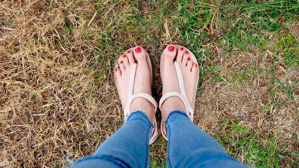 Pés Selfie em sandálias em pé sobre grama verde e grama seca fundo — Fotografia de Stock