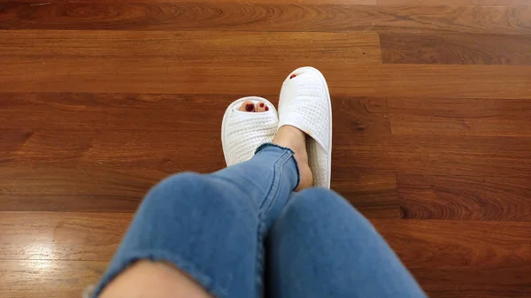 Pés de menina usam chinelos brancos e jeans azuis no fundo do piso de madeira — Fotografia de Stock