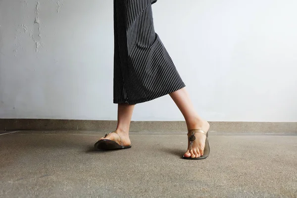 Piedi Donna indossare sandali e pantaloni neri. Donna in piedi sullo sfondo di cemento — Foto Stock