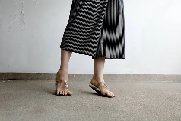 Γυναίκα πόδια φορούν σανδάλια και μαύρο παντελόνι. Γυναίκα που στέκεται πάνω σε υπόβαθρο τσιμέντο — Φωτογραφία Αρχείου