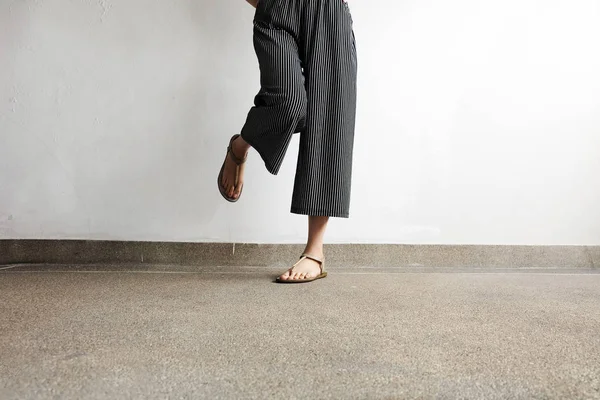 足女は、サンダルと黒ズボンを着用します。セメントの背景に立っている女性 — ストック写真