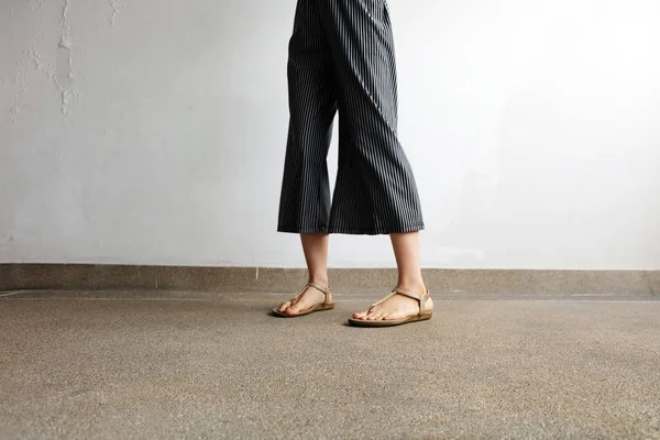 Les pieds femme portent des sandales et des pantalons noirs. Femme debout sur le fond de ciment — Photo