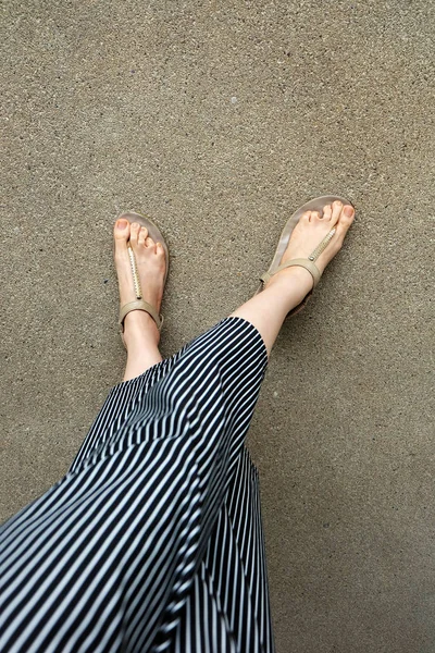 Feet Woman Wear Sandals and Black Pants. Female Standing on The Cement Background
