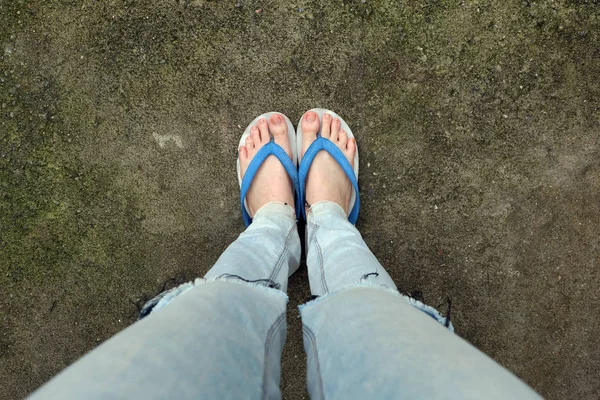 Ung kvinna ben i blå sandaler och blå Jeans. Kvinna som står på Cement bakgrunden — Stockfoto