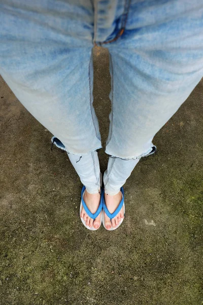 Νεαρή γυναίκα πόδια σε μπλε πέδιλα και μπλε τζιν. Γυναίκα που στέκεται πάνω σε υπόβαθρο τσιμέντο — Φωτογραφία Αρχείου