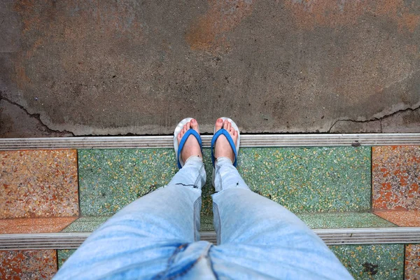 Ноги молодой женщины в синих сандалиях и синих джинсах. Женщина стоит на заднем плане цемента — стоковое фото