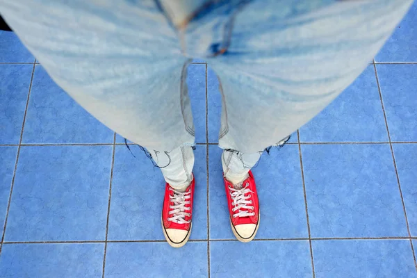 Sport röda Sneakers, nära upp kvinna ben i röda Sneakers och blåjeans står på blå-bildrutsbakgrund — Stockfoto