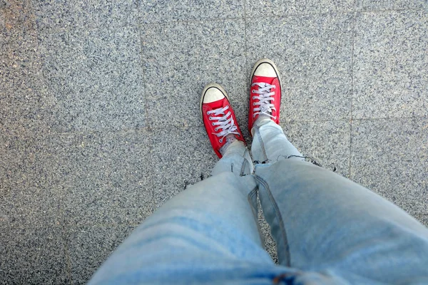Sport röda Sneakers, kvinna ben i röda Sneakers och blåjeans står på Cement bakgrunden — Stockfoto
