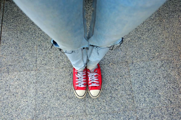 Esporte tênis vermelhos, pernas de mulher em tênis vermelhos e jeans azuis em pé no fundo do cimento — Fotografia de Stock