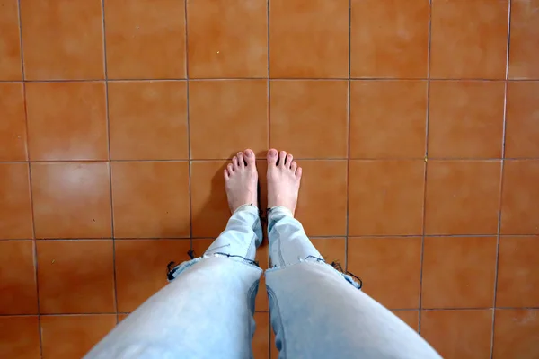 Close Up Donna a piedi nudi indossare jeans blu su sfondo mattonelle marrone — Foto Stock