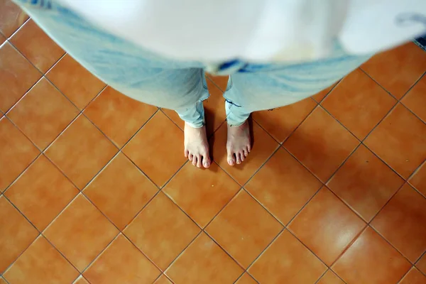 Kobieta boso nosić niebieskie dżinsy na tle brązowy dachówka z bliska — Zdjęcie stockowe
