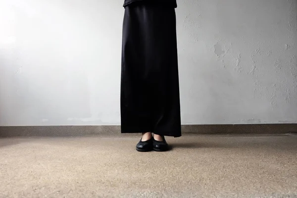 Pies de luto hembra en zapatos planos negros y vestido negro de pie sobre el fondo de hormigón —  Fotos de Stock