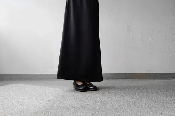 Smuteční nohy žena v černých šatech, stojící na konkrétní pozadí a černé ploché boty — Stock fotografie