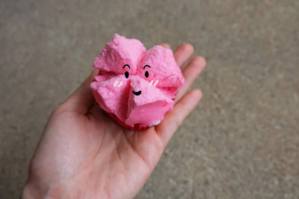 Στενή επάνω στον ατμό κέικ φλυτζανιών, χέρι κρατήστε ροζ στον ατμό κέικ κύπελλο με χαμόγελο πρόσωπο σε σκυρόδεμα φόντο — Φωτογραφία Αρχείου
