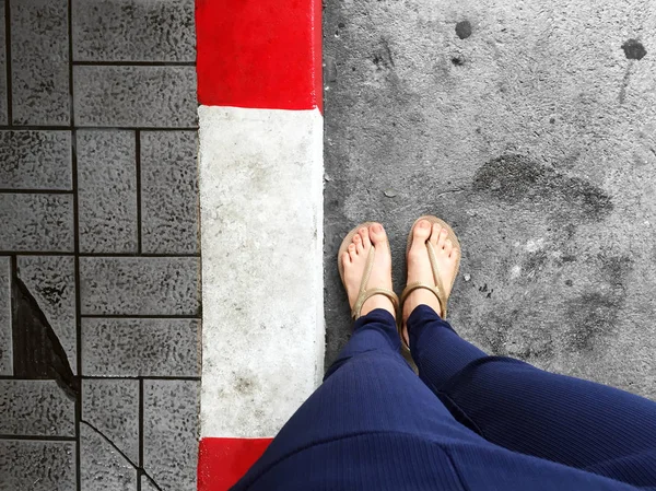 Женские ноги носить сандалии стоят красный и белый бетон бордюр, бетонная дорога - тротуар для заднего плана — стоковое фото