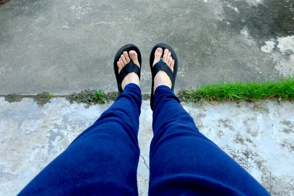 Frauensandale. Füße Selfie in schwarzen Sandalen mit blauer Hose auf dem Boden stehend Hintergrund — Stockfoto