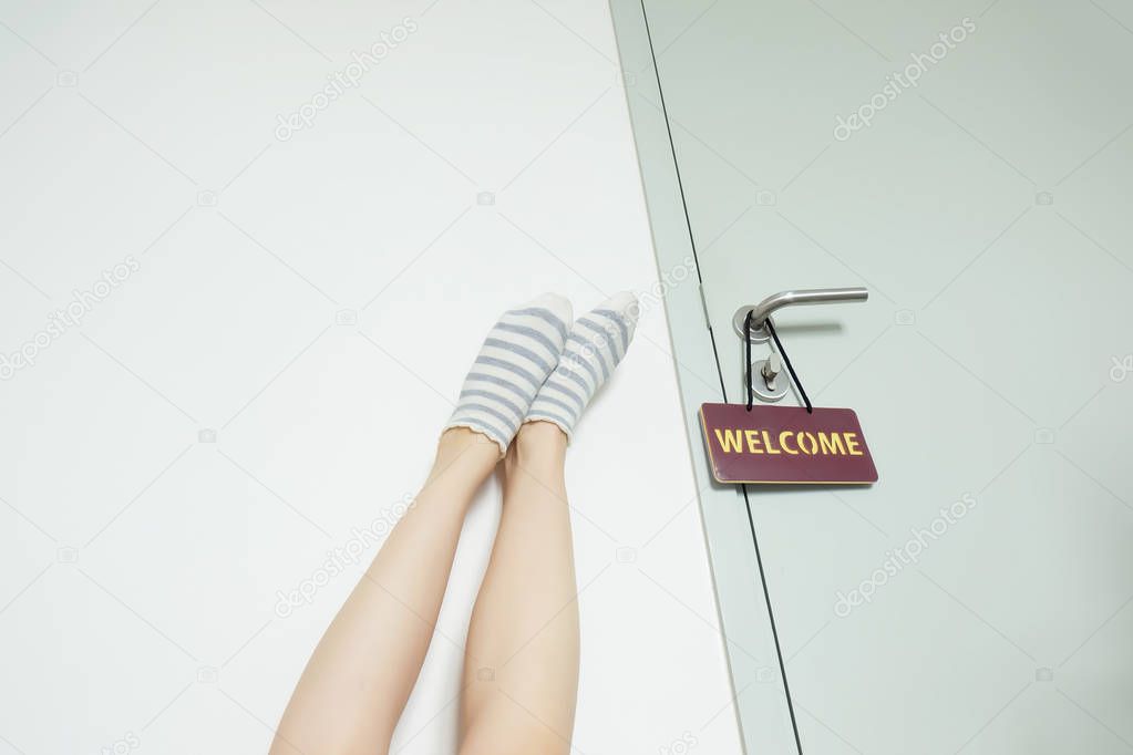 Slim Legs. Woman's Legs in Striped Yellow socks Near Door with Label Welcome on White Wall at Home