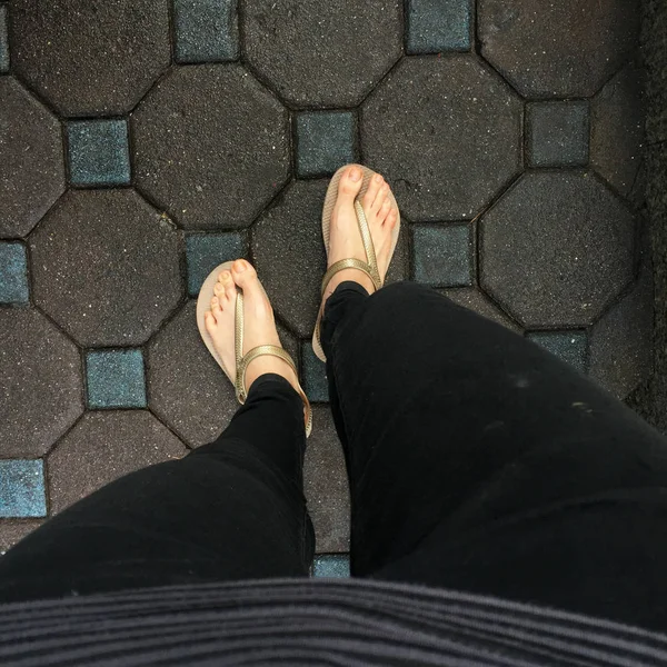 Selfie Woman\'s Feet Wearing Sandals and Black Jeans on Tile Background