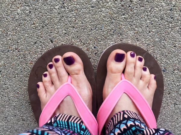 Sandalia, de cerca en las uñas y pies violetas de la muchacha con sandalias rosadas en el fondo del piso de cemento — Foto de Stock