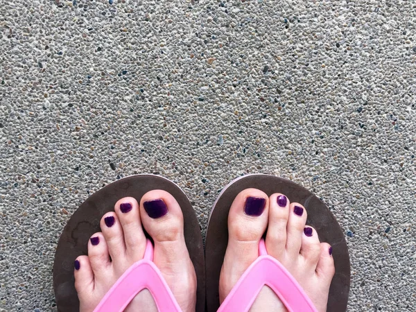 Sandalia, de cerca en las uñas y pies violetas de la muchacha con sandalias rosadas en el fondo del piso de cemento — Foto de Stock