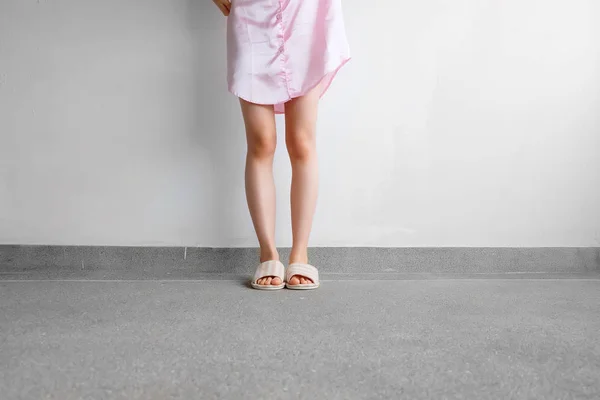 Дівчина стоїть у сплячому одязі та рожевих картатих тапочках з триманням рожевої подушки на підлозі — стокове фото