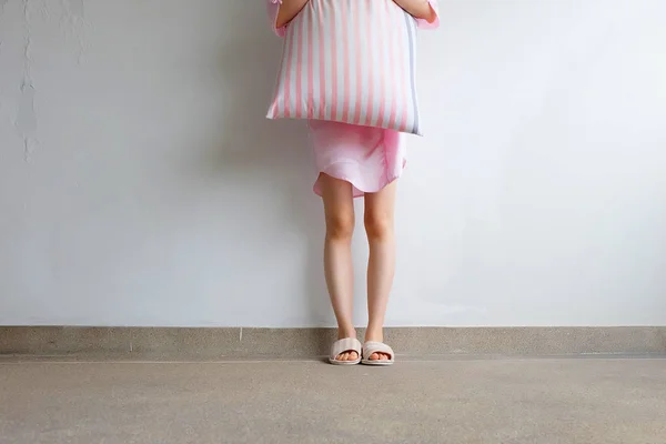 女孩站在睡衣和粉红色的格子拖鞋, 在地板上抱着粉红色的枕头 — 图库照片
