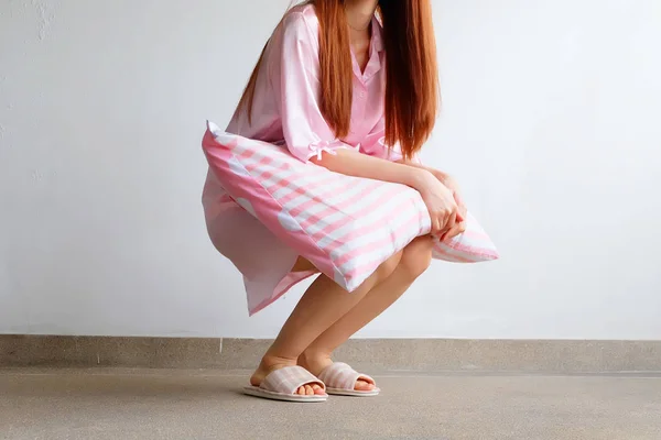 Chica de pie en ropa de dormir y zapatillas de cuadros rosa con la celebración de almohada rosa en el piso — Foto de Stock