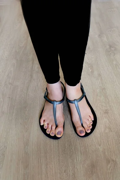 Pernas de menina e pés usam sandálias pretas no fundo de madeira — Fotografia de Stock