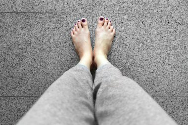 Çivi pedikür ile barefeet. Yakın kadının bacakları gri döşeme arka planı üzerinde duran gri pantolon giymek