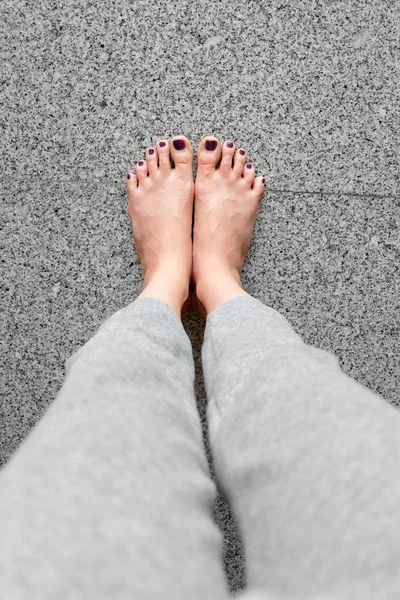 赤脚与指甲修脚。近距离女腿穿灰色裤子站在灰色瓷砖背景 — 图库照片