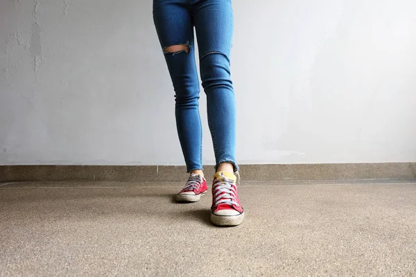 Zapatillas rojas. Piernas de mujer en zapatillas de deporte rojas y pantalones vaqueros azules en el fondo del piso —  Fotos de Stock