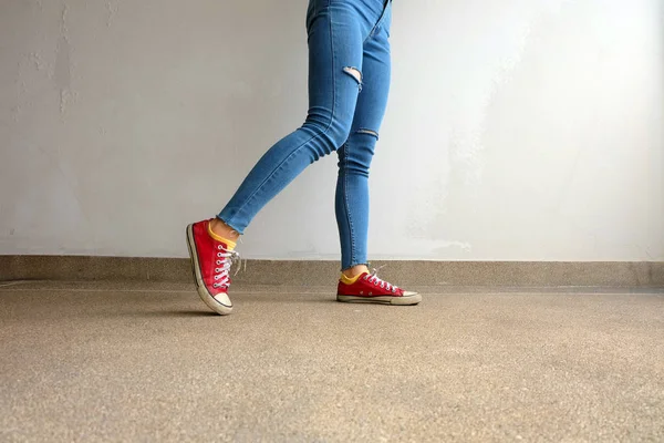 Zapatillas rojas. Piernas de mujer en zapatillas de deporte rojas y pantalones vaqueros azules en el fondo del piso — Foto de Stock